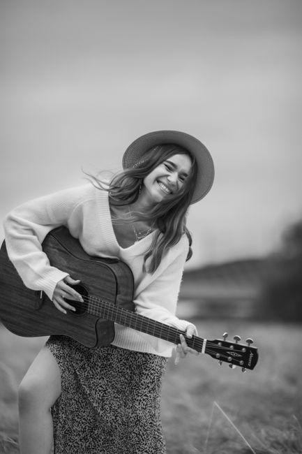 Cheerful woman with a hat playing guitar, enjoying leisure in a natural setting.