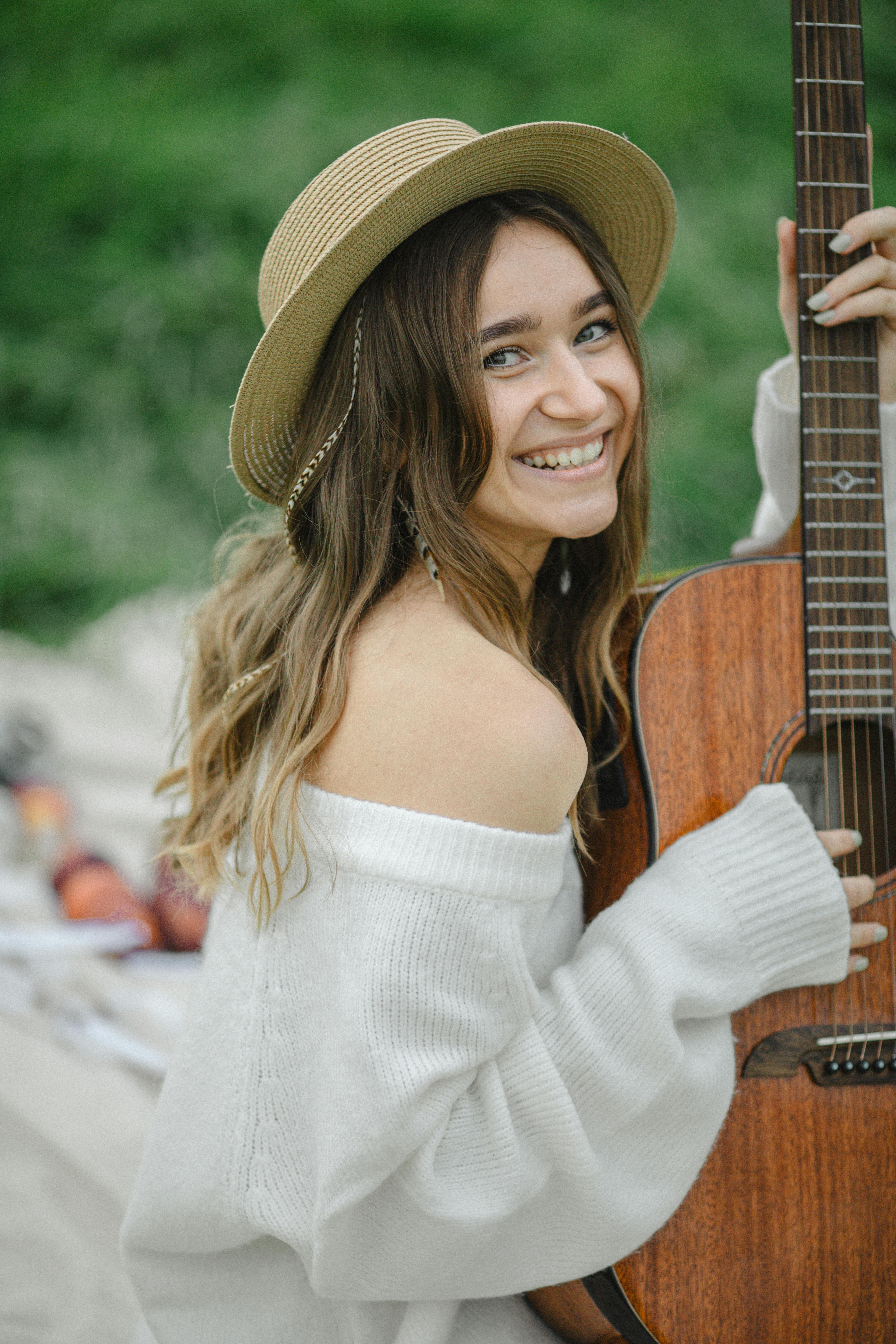Smiling woman in a hat holding a guitar outdoors in a field.