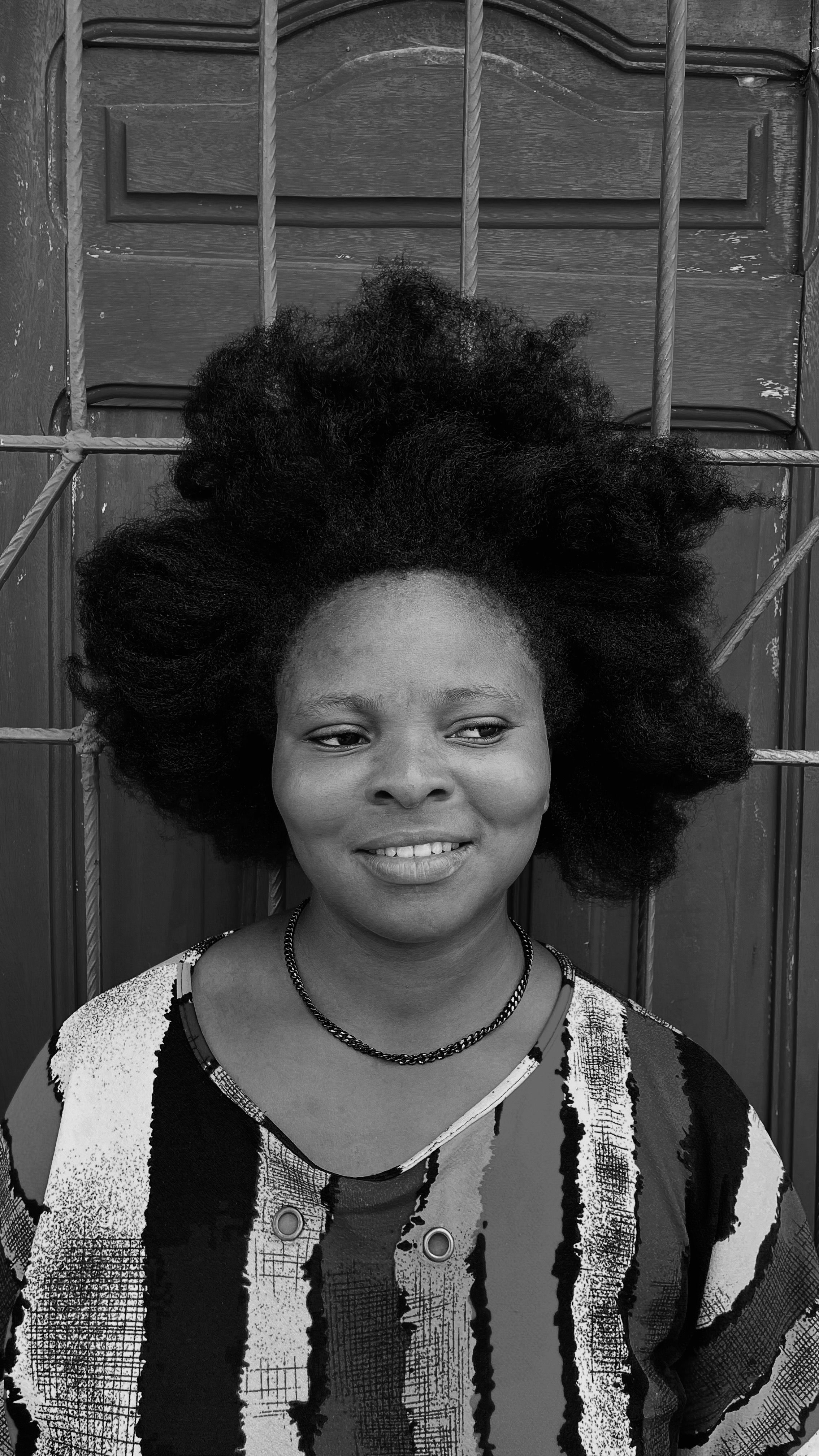 Black and white portrait of a smiling woman with afro hairstyle standing in Accra, Ghana.