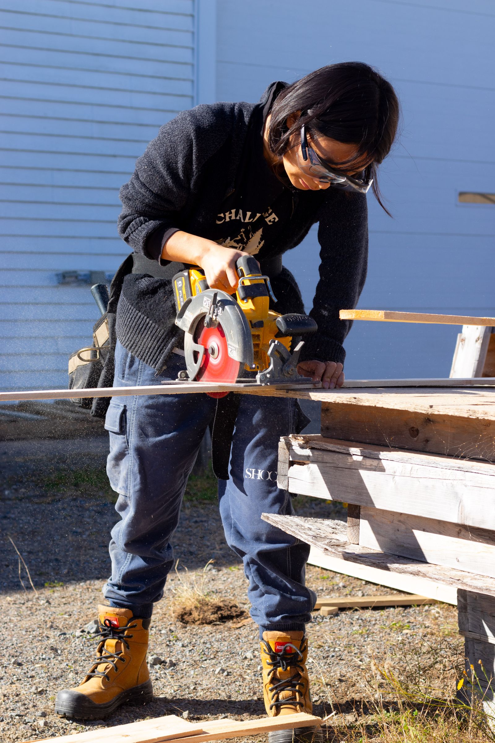 Carpenter wearing protective goggles while cutting a wooden plank with a circular saw