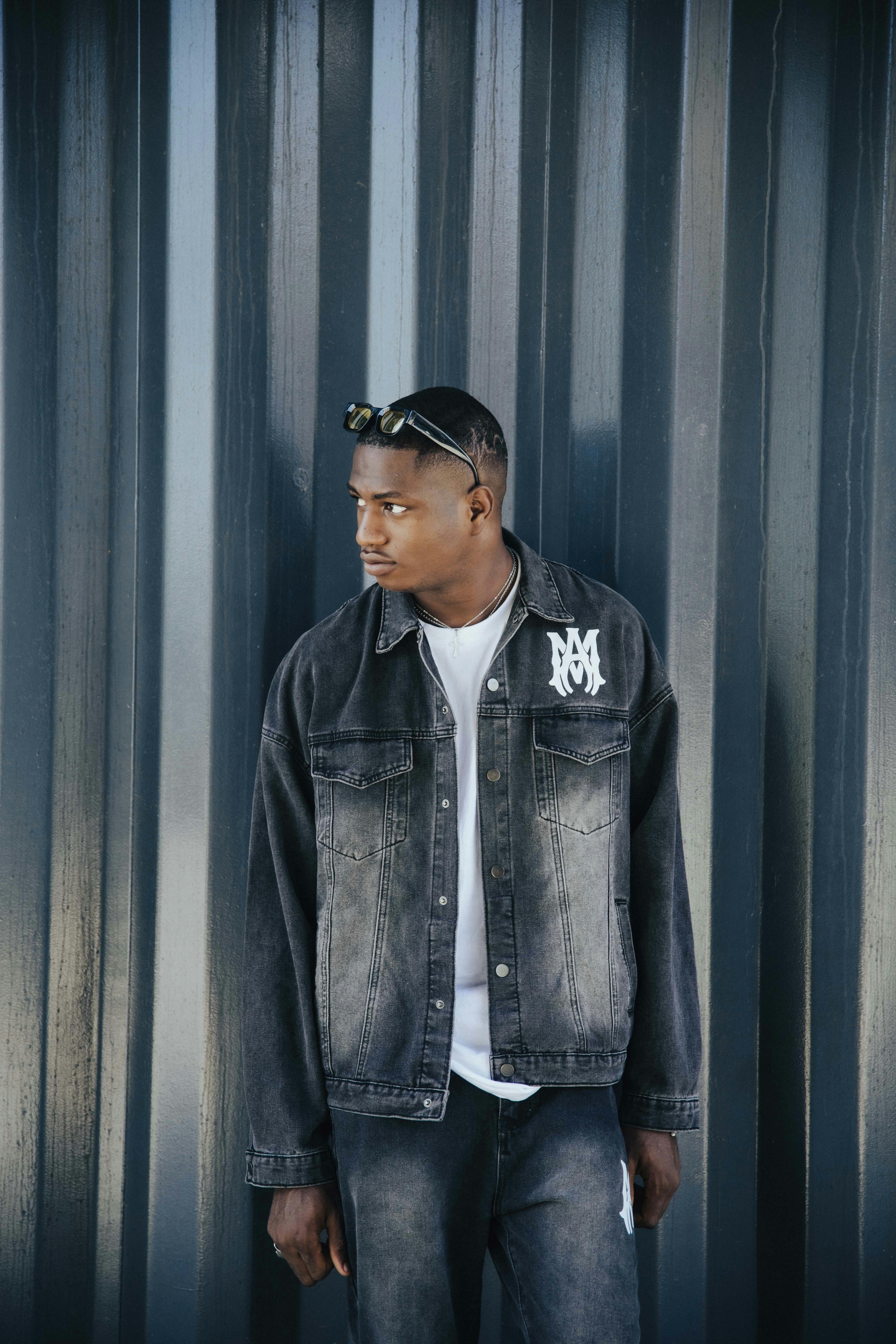 Young man in a denim jacket standing against a modern metallic wall, exuding casual fashion vibes.