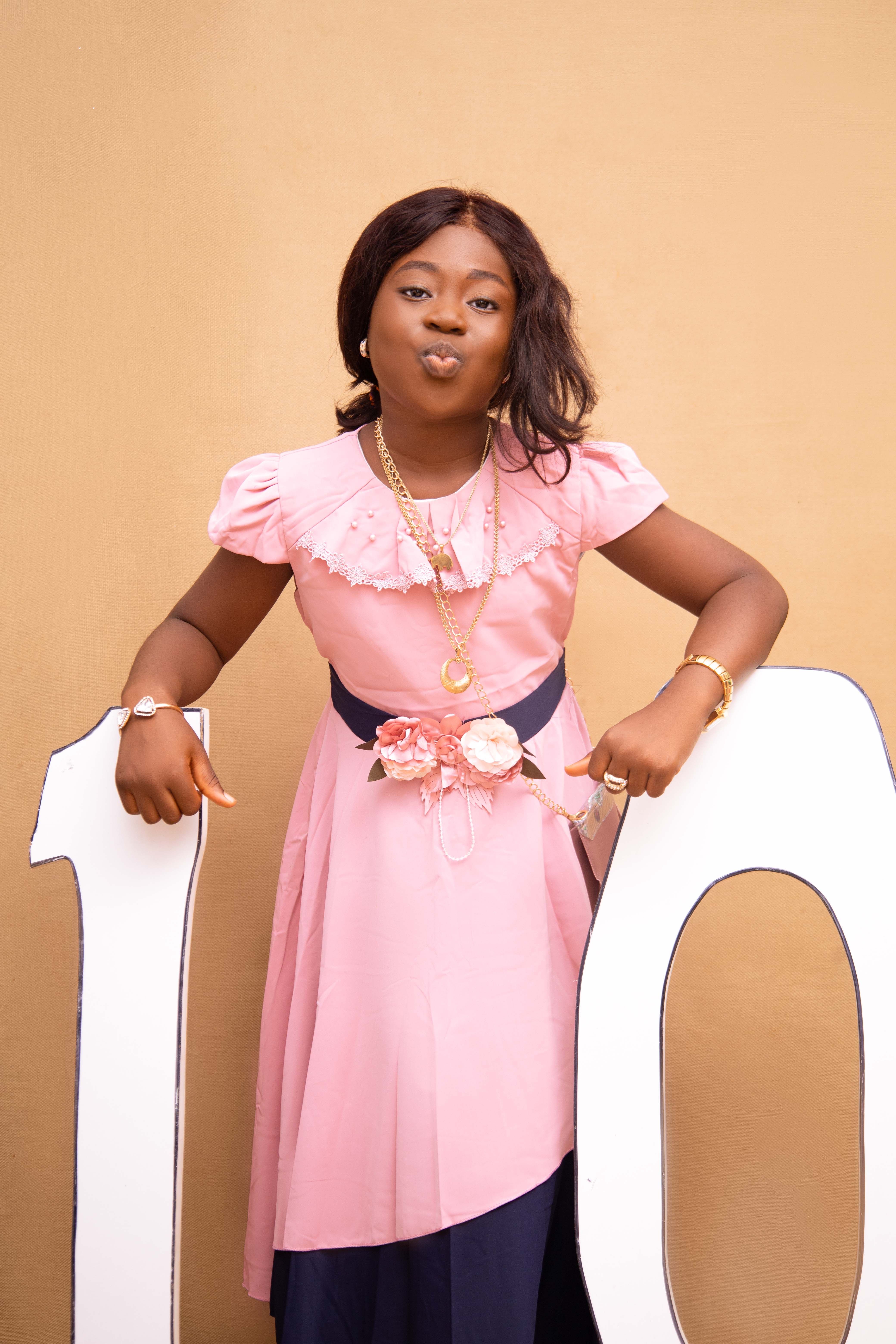 A young girl in a pink dress celebrating her 10th birthday with a playful pose.