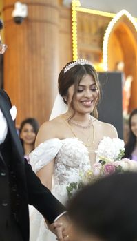 A happy bride dressed in a beautiful white gown smiles during a wedding ceremony indoors.