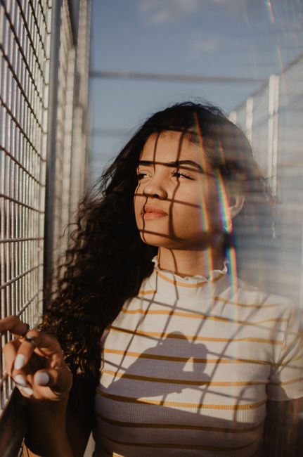 Stylish portrait of a woman with curly hair in sunlight, creating a grid shadow pattern on her face.
