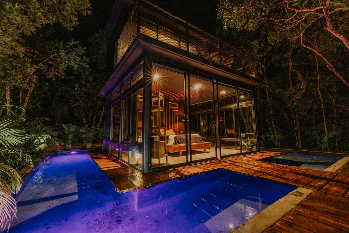 A glass-walled house glowing over a dark pool at night