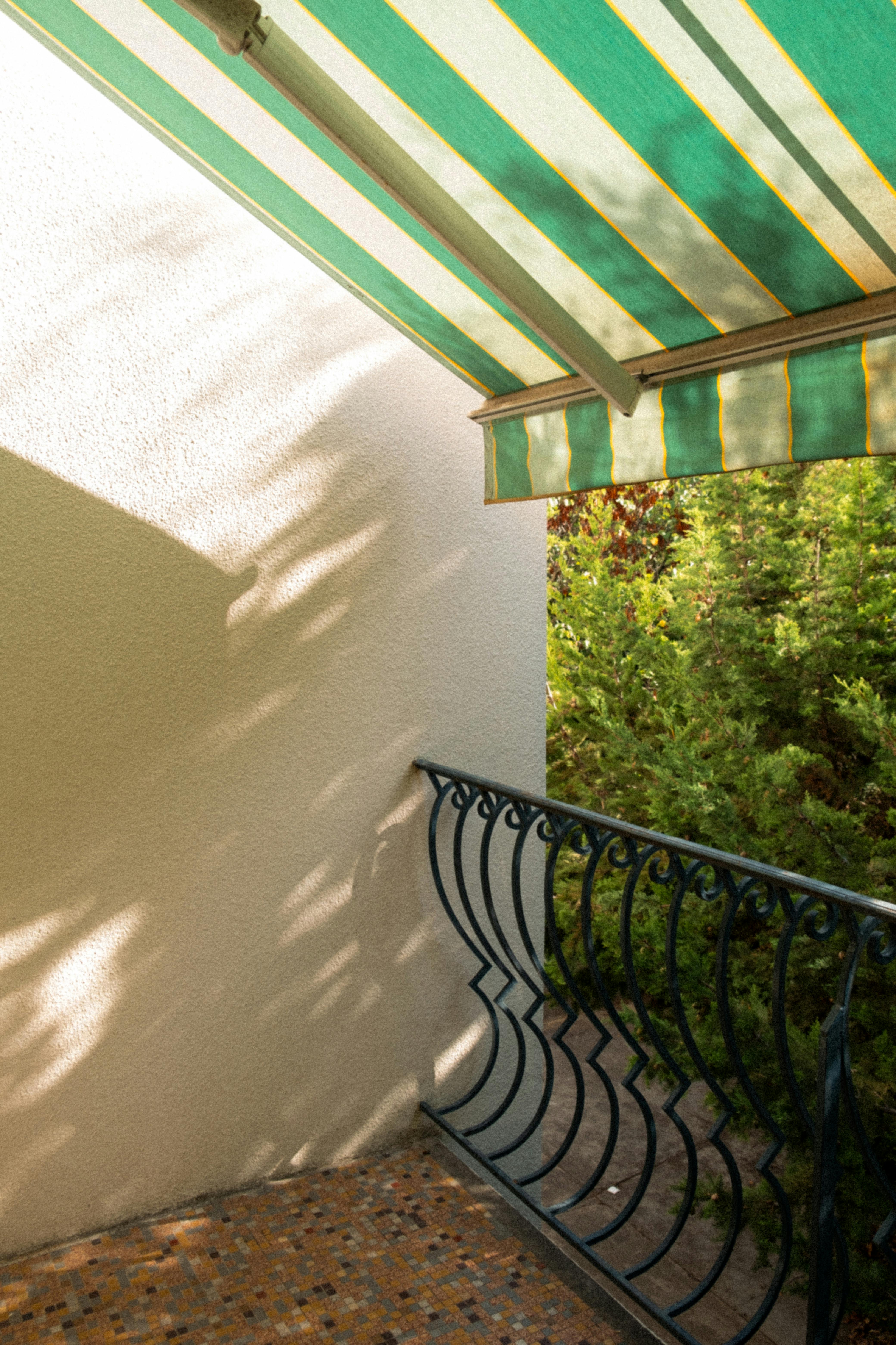 A sunlit balcony featuring a green striped awning and a decorative railing.