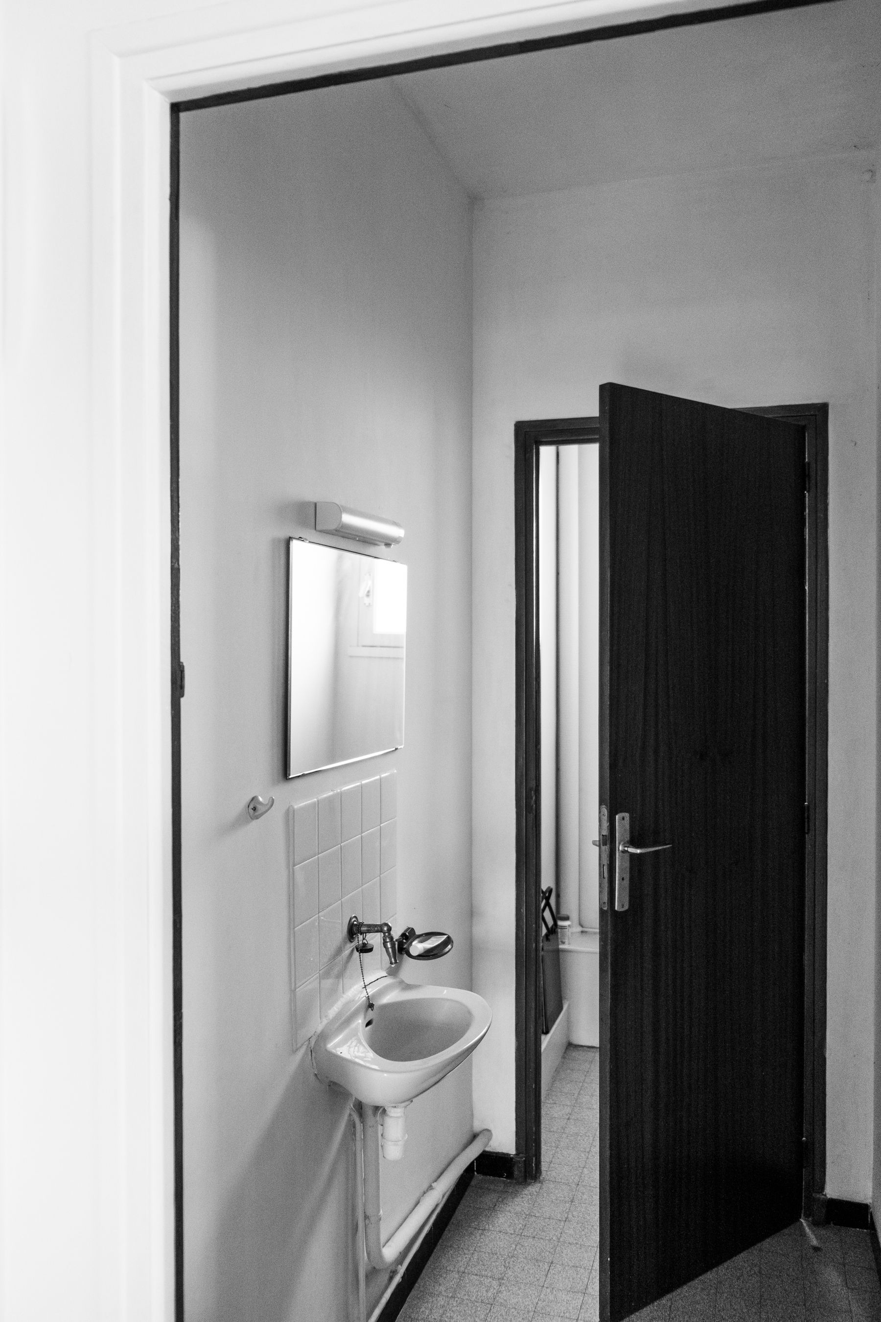 Simple black and white bathroom with white walls, dark floor and wood door