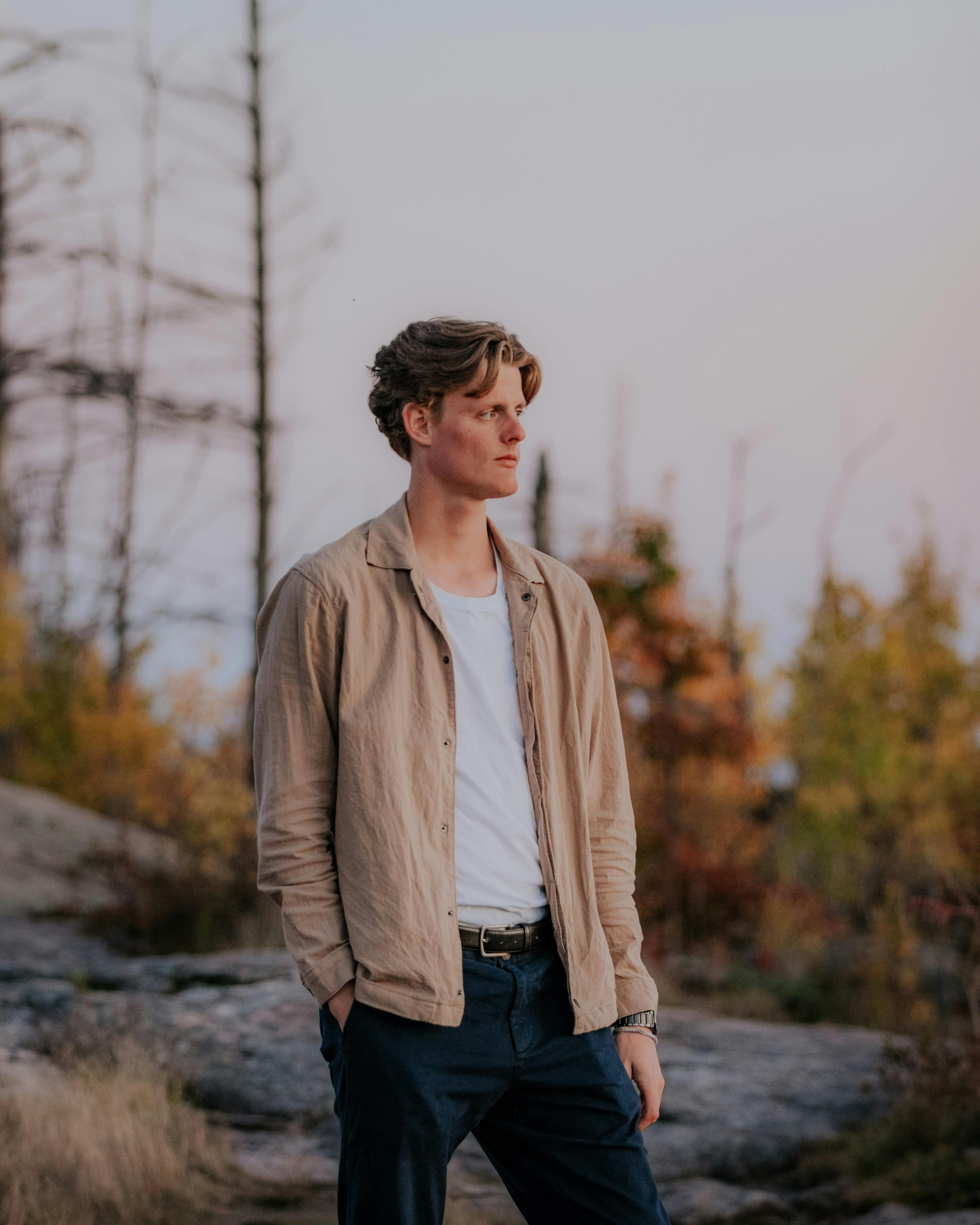 A young man in a beige jacket gazes thoughtfully in an autumn forest setting.