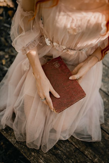 A woman gracefully poses with an old book, wearing a flowing tulle dress, creating a timeless fashion scene.