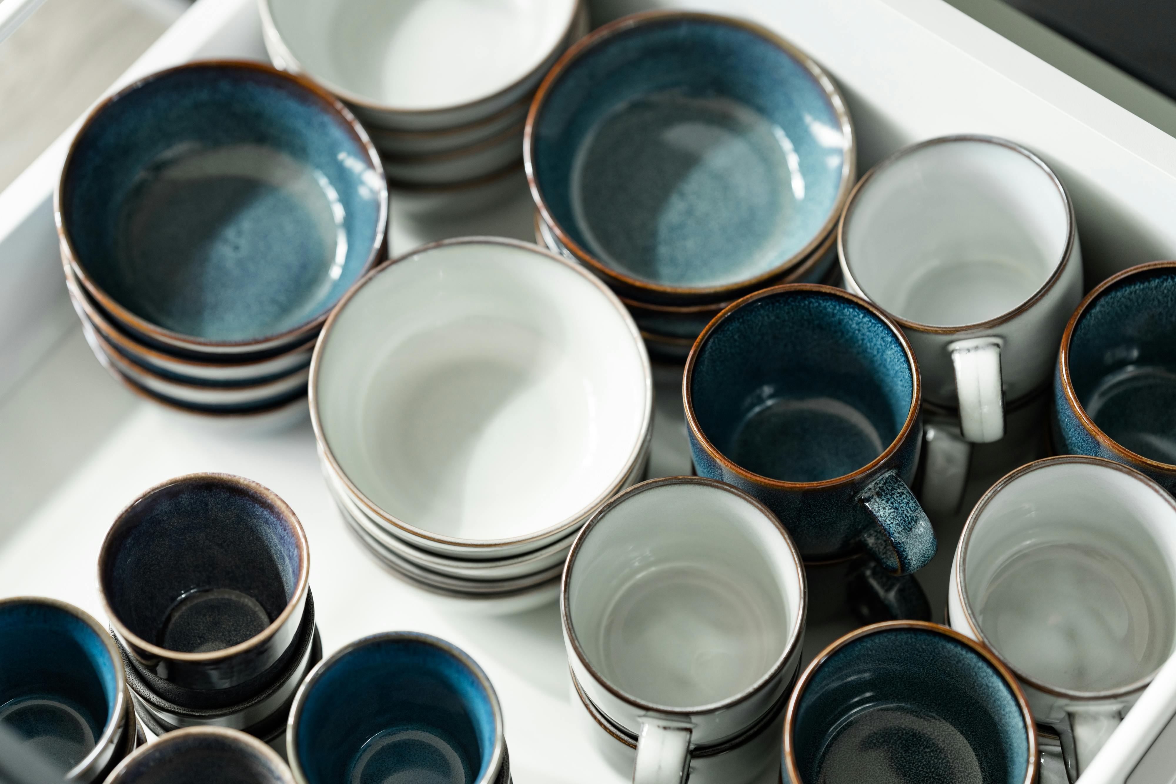 Close-up of stacked ceramic bowls and cups with blue glaze in a drawer.