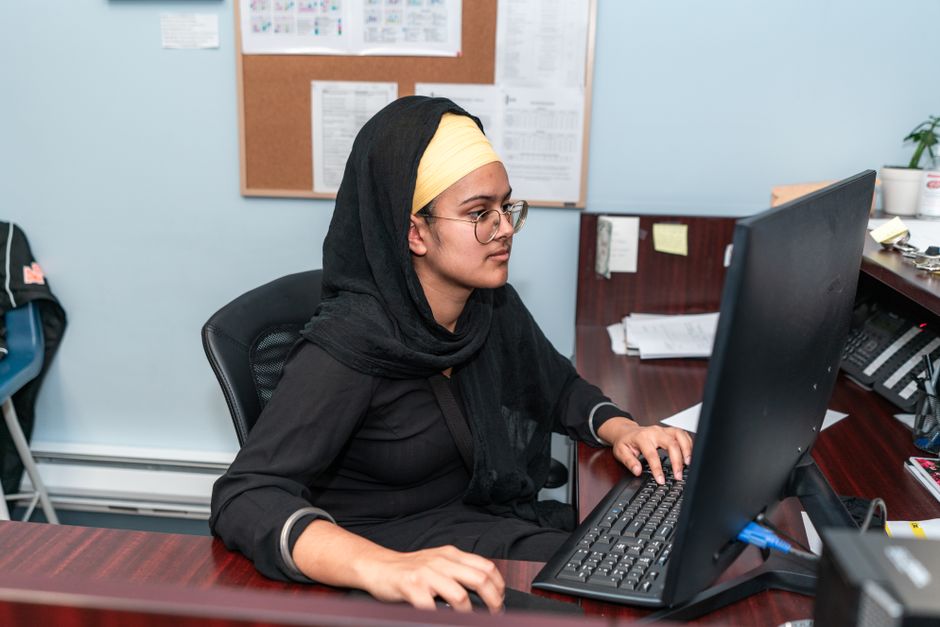 Middle Eastern woman in hijab using computer in office setting, focusing on work.