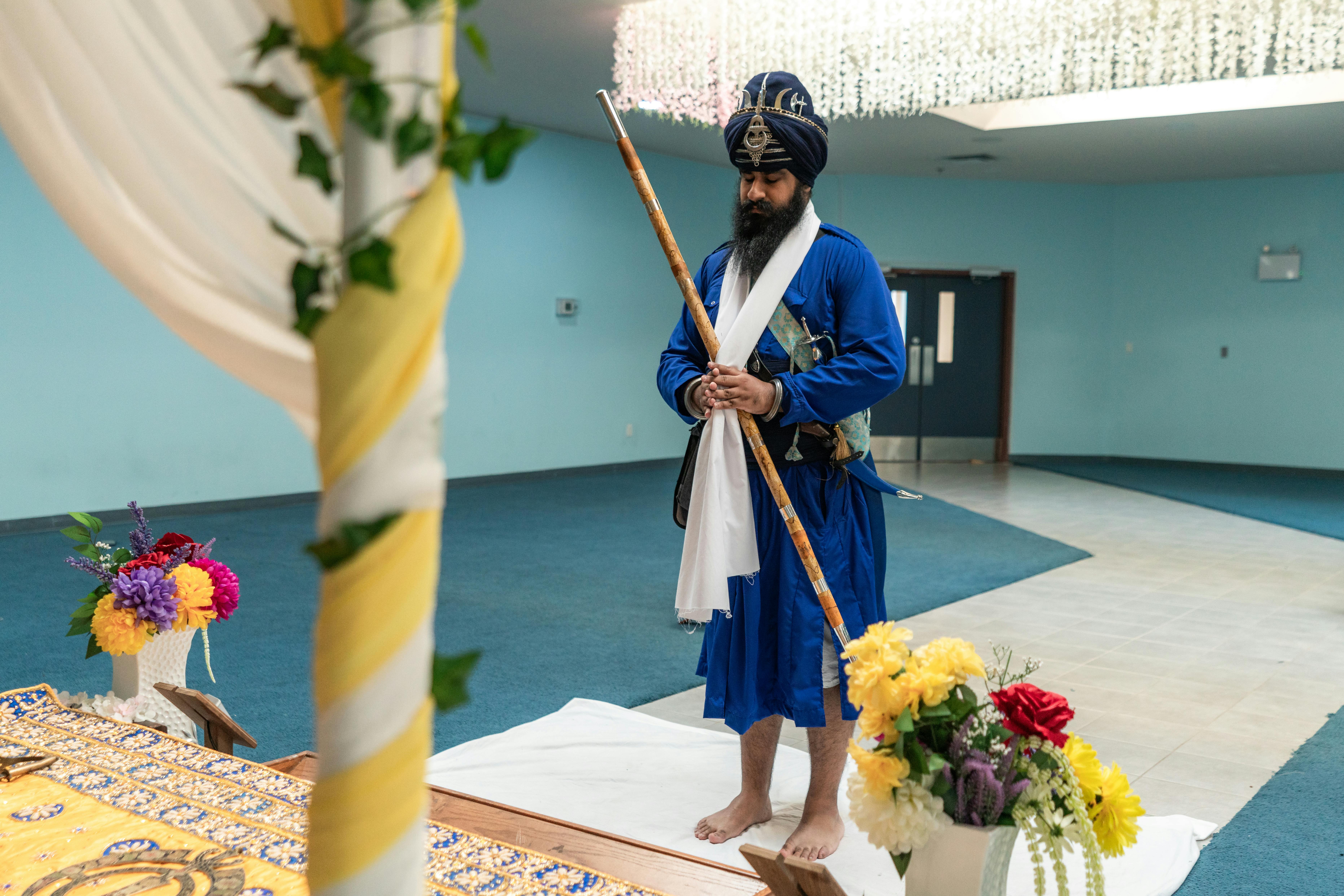 A Sikh man in blue traditional attire participates in a cultural ceremony indoors.