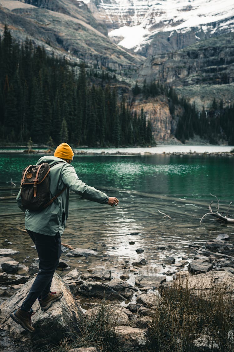 Man Walking On Rocks By Lake In Mountains