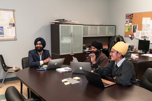 A diverse group of professionals having a meeting in an office setting, using laptops and engaging in teamwork.