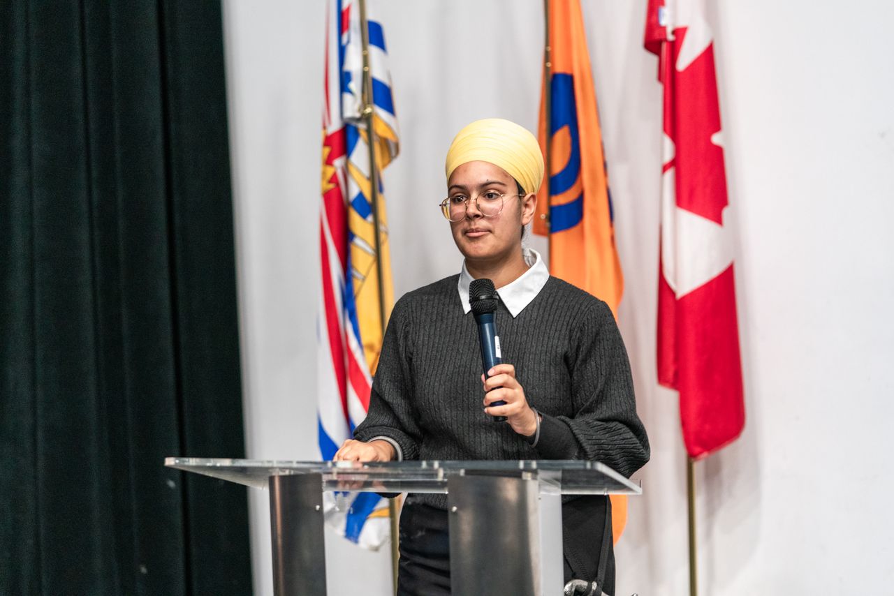a young woman wearing a turban speaks at a podium with international f