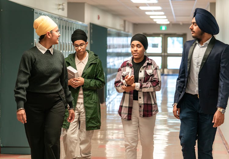 Student Talking With Teachers Walking Along A School Corridor