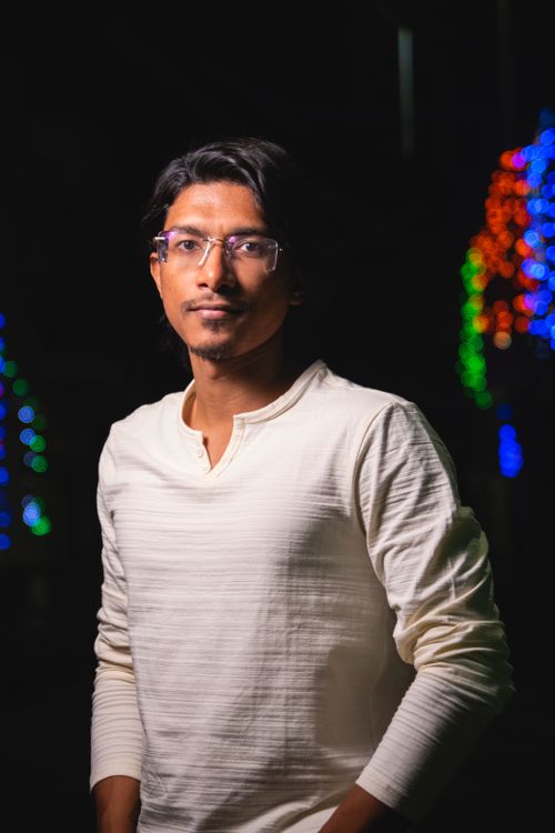 Free A stylish young man with glasses poses at night with colorful lights in the background. Stock Photo