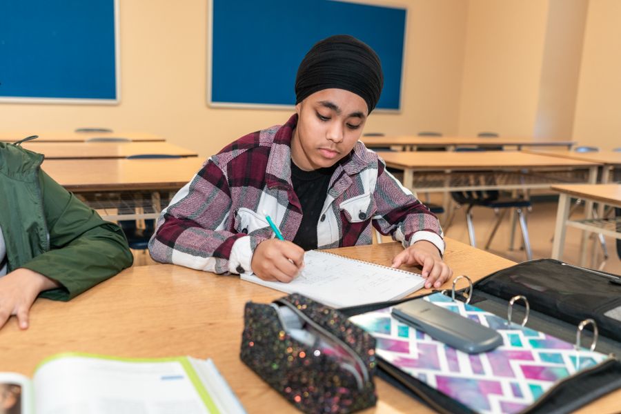 Teenage student writing at a desk in a classroom, focusing on learning and education.