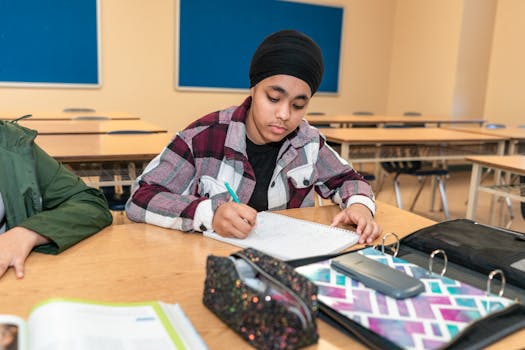 Teenage student writing at a desk in a classroom, focusing on learning and education.