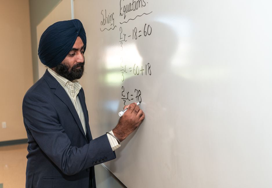 understanding the balance sheet equation for clarity - Man in turban teaching mathematics, solving equations on a whiteboard indoors.