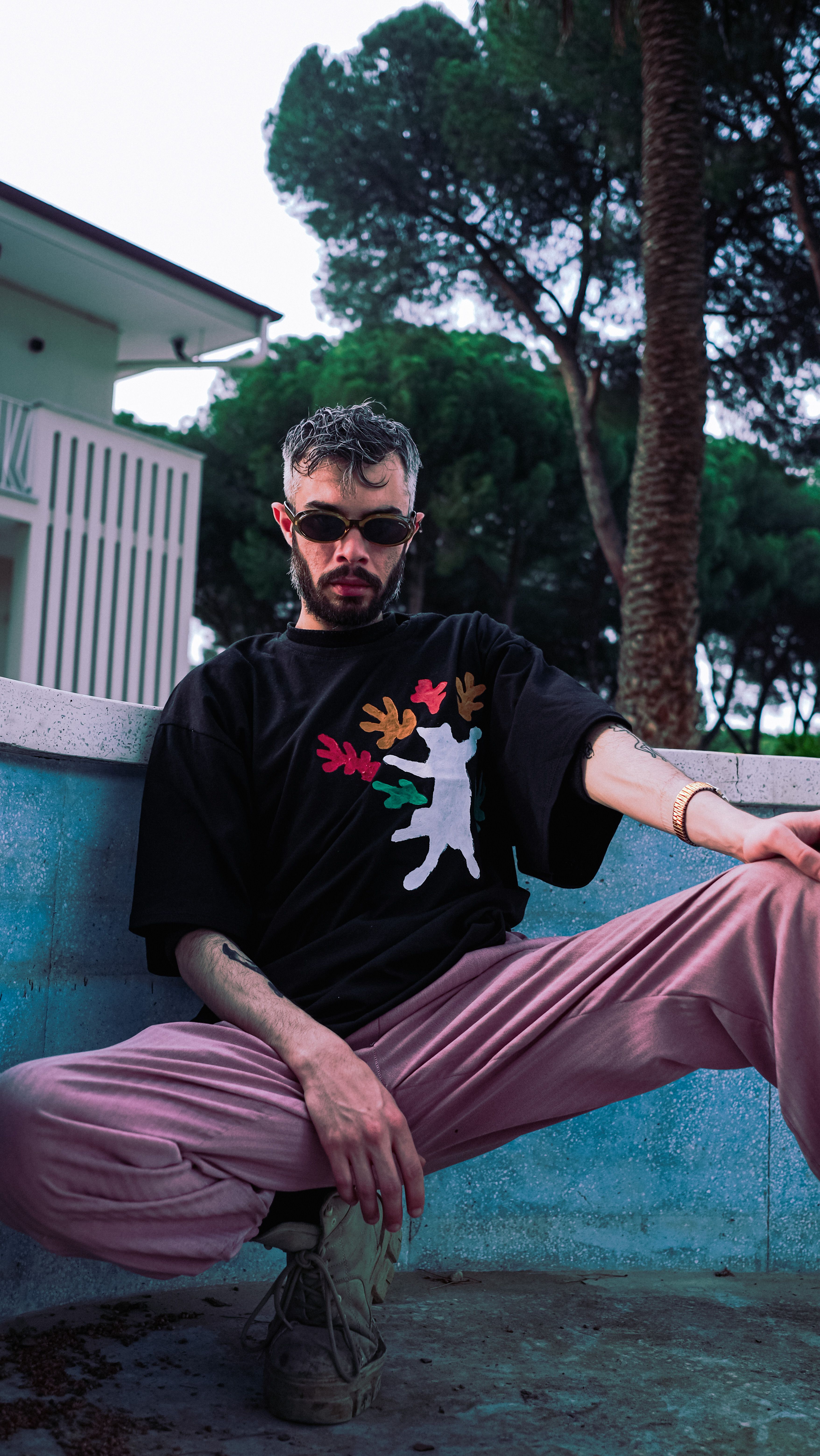 Fashionable man in pink pants and sunglasses posing outdoors with a cool vibe.
