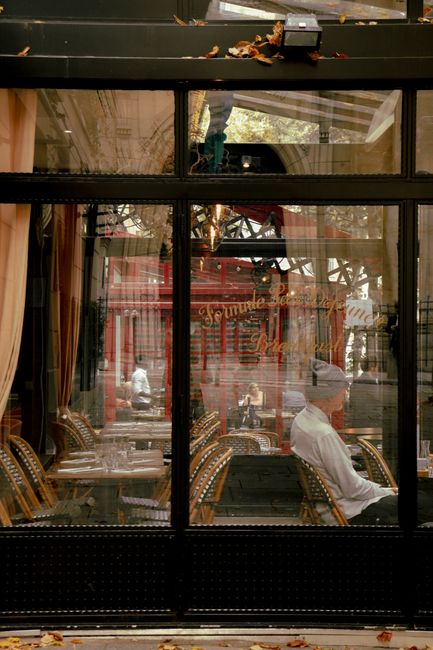 Chic Paris café interior seen through a reflective window, showcasing elegant decor and cozy seating.