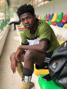 A young athlete sits on colorful stadium bleachers wearing sportswear, contemplating the game.