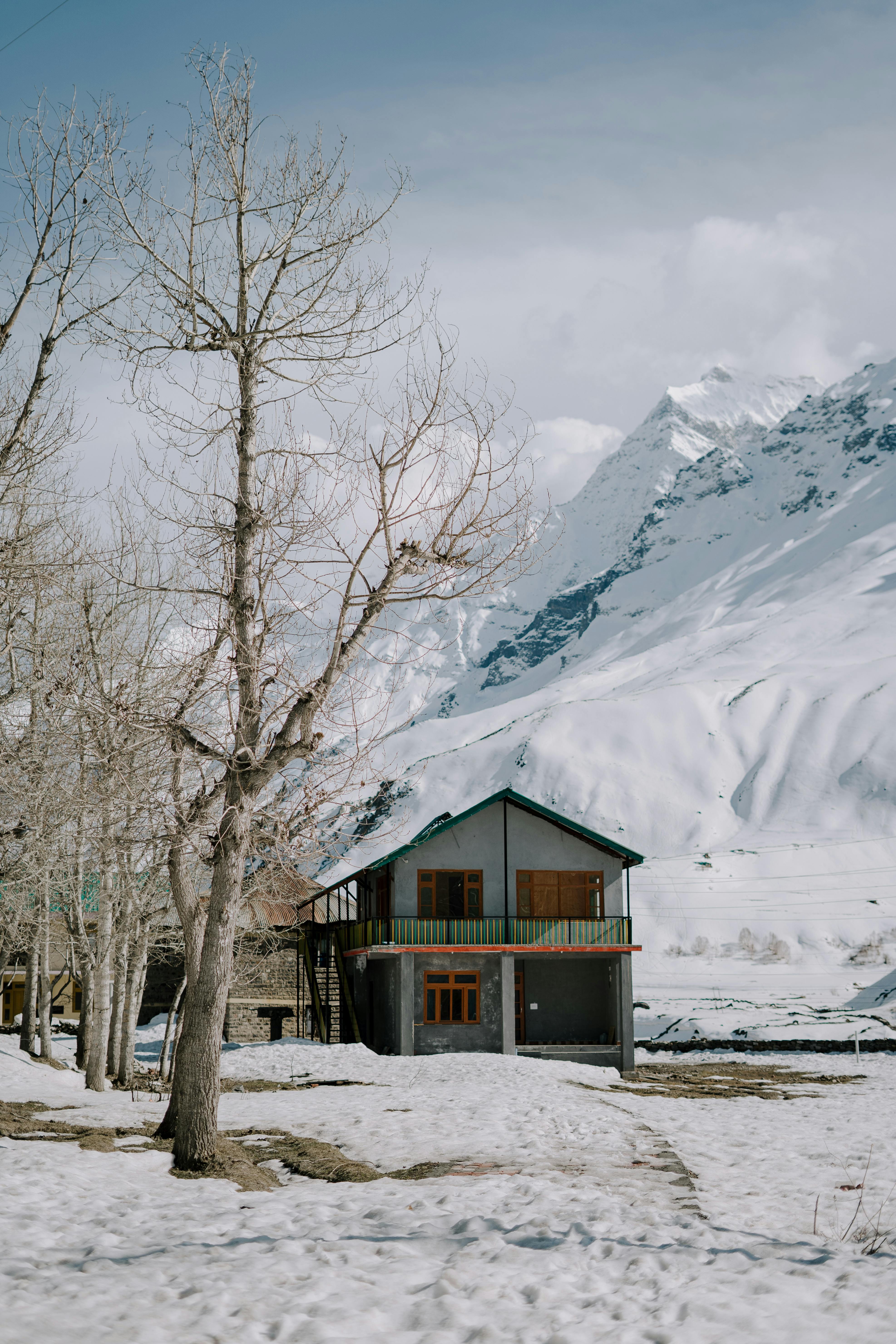 A picturesque rural house surrounded by snow and mountains, capturing the serene winter landscape.