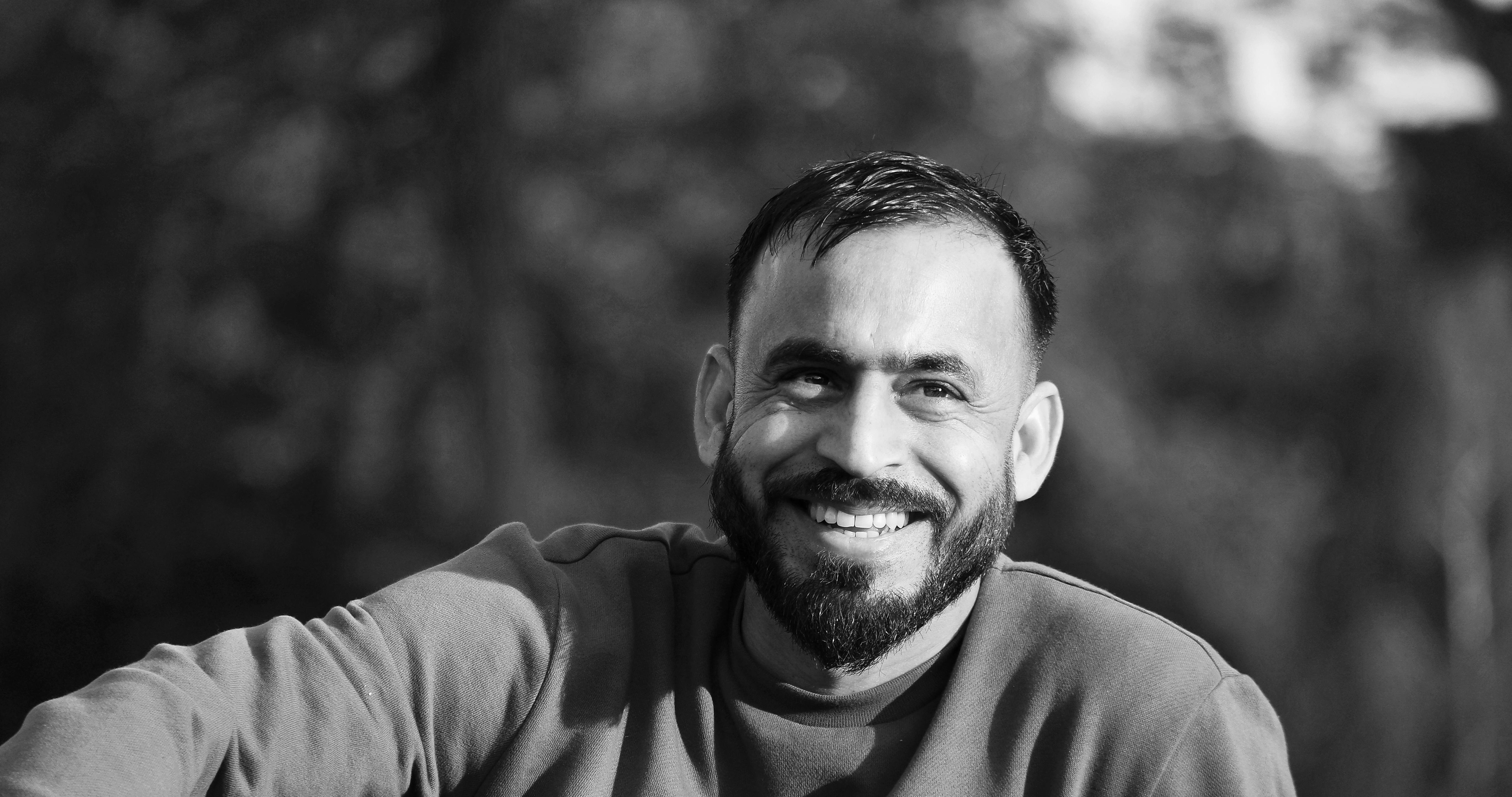 A black and white portrait of a smiling man with a beard in an outdoor setting.