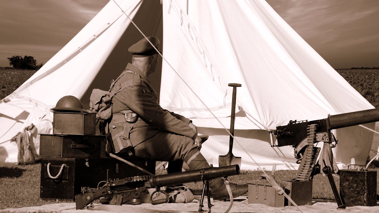 無料 銃と白いガゼボの近くに座っている軍服を着た男のセピア写真 写真素材