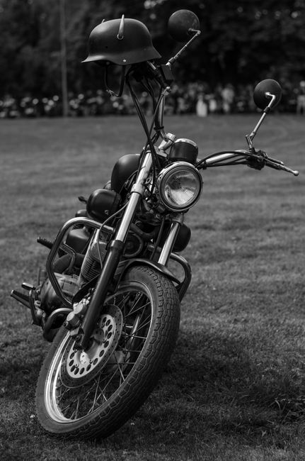 Classic black and white photo of a vintage motorcycle with a helmet parked on a grassy field.