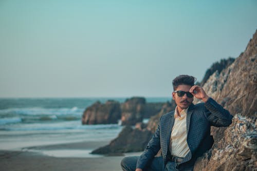 Young Man in a Suit and Sunglasses Sitting on the Beach 