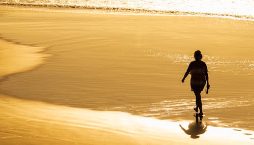 Woman Walking on Sunlit Sea Shore