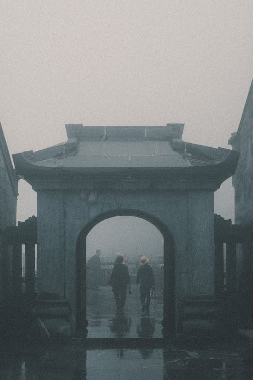 People Walking behind Temple Gate under Fog