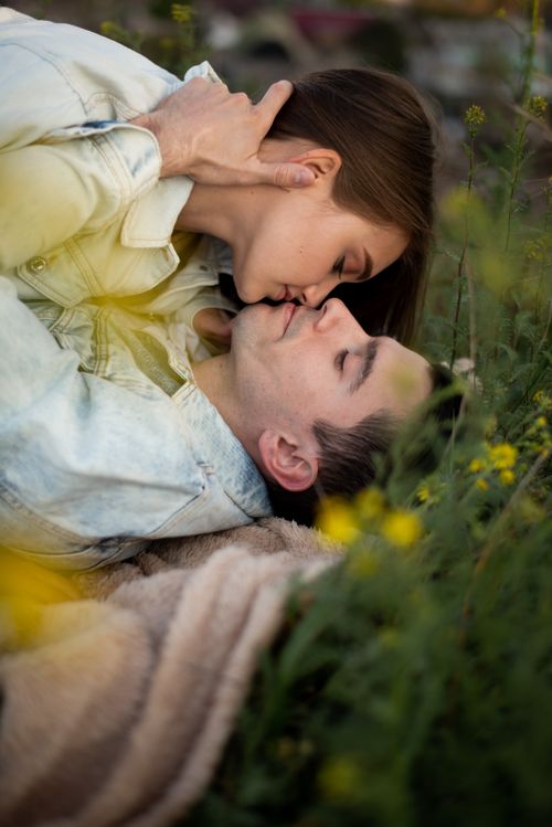 Free A couple kisses among yellow flowers in a meadow, depicting love and intimacy outdoors. Stock Photo