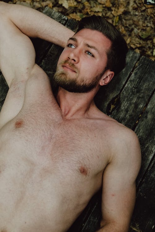 Shirtless Man Lying on top of a Picnic Table
