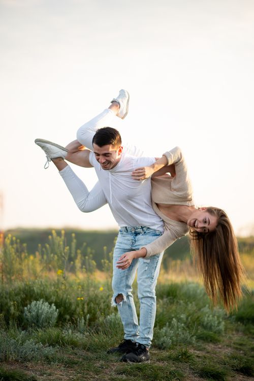 Free A young couple enjoying playful moments in a sunny, grassy field. Stock Photo