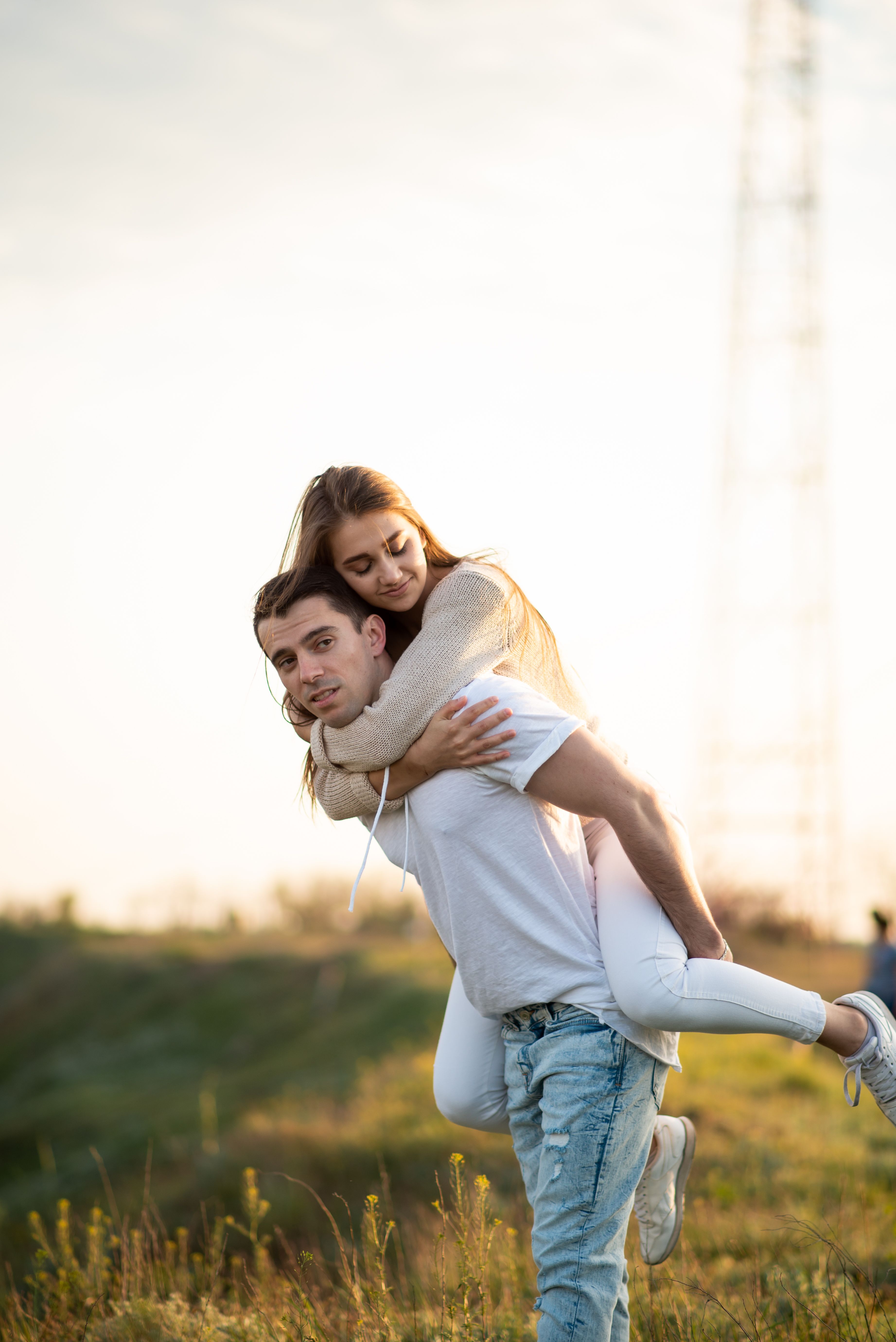 A joyful couple enjoying a piggyback ride in a sunlit rural field, embodying happiness and love.