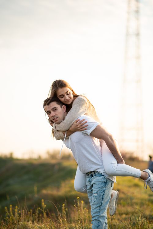 Free A joyful couple enjoying a piggyback ride in a sunlit rural field, embodying happiness and love. Stock Photo