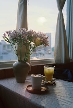 A cozy table setting with coffee, juice, and flowers by a sunlit window.