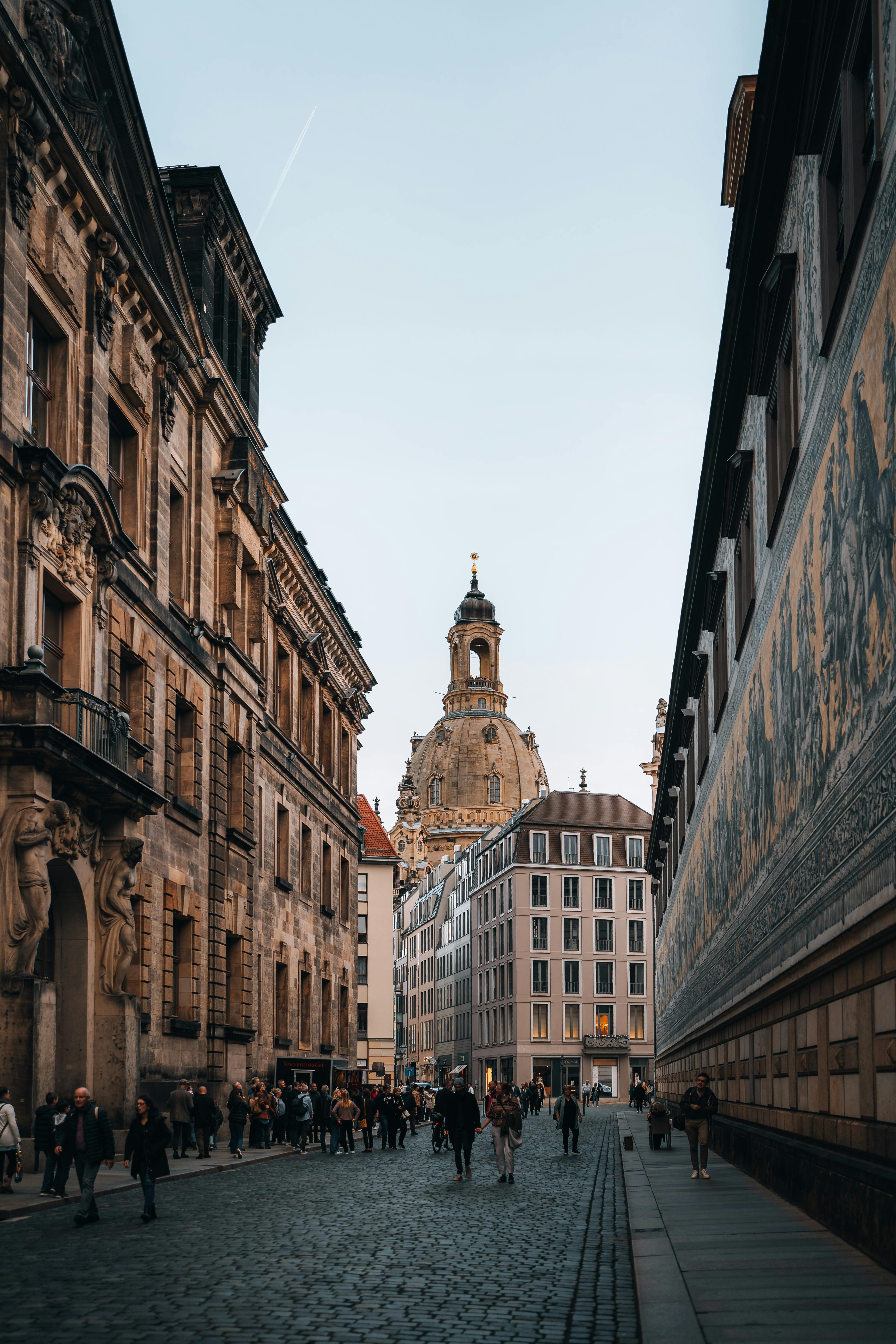View of a busy cobblestone street in Dresden featuring the Frauenkirche dome, lined with historic buildings.