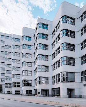 A cityscape featuring a modern building with a unique curved white facade and numerous windows.