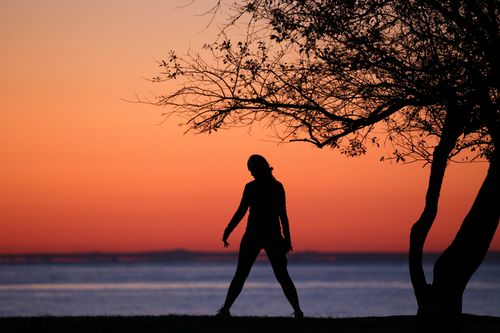 Free A serene silhouette of a person standing by the ocean during a vibrant sunset. Stock Photo