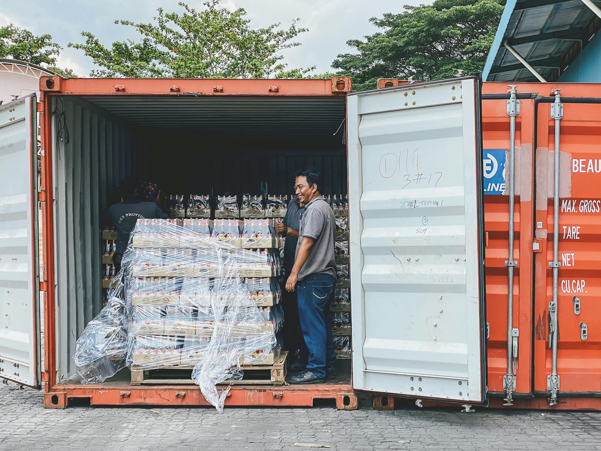 Two men load products into a shipping container in Ipoh, Malaysia, showcasing logistics.