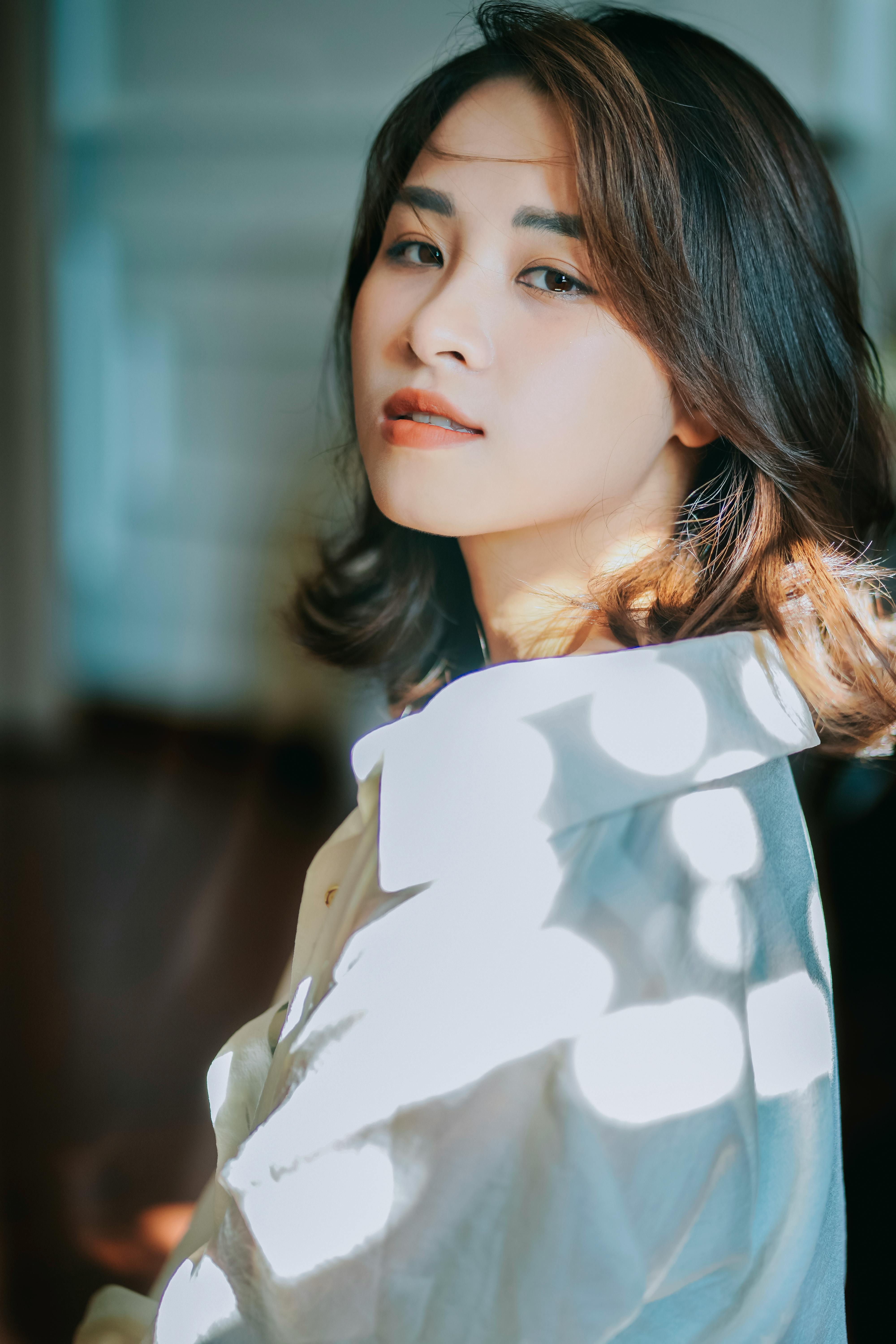 A beautiful young woman in a white shirt posing gracefully in sunlit indoors.