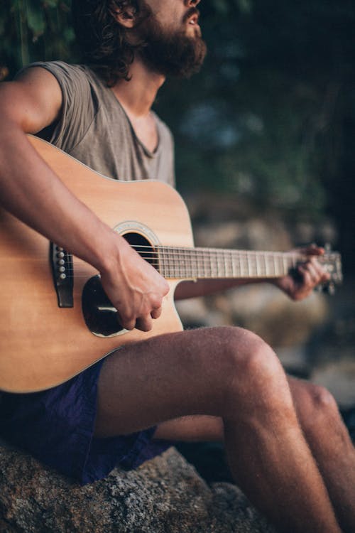 Man Sitting on Rock Playing Guitar