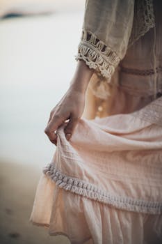 在海滩边，一名女子手持飘逸的波西米亚连衣裙，捕捉着宁静的时刻