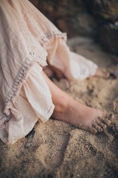 A barefoot woman in a flowing dress standing on a sandy beach, capturing a serene moment.