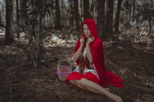 Free Woman in red cloak as Red Riding Hood, sitting barefoot in a forest with a basket. Stock Photo
