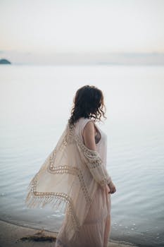 一位身着飘逸连衣裙的女子凝视着宁静大海，这一刻被捕捉下来